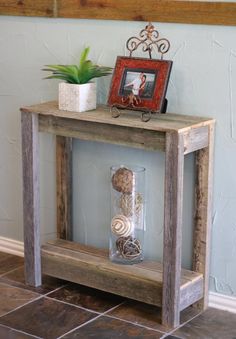 a wooden table with an empty vase on top and a framed picture in the middle