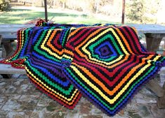 a multicolored crocheted blanket sitting on top of a wooden bench next to a picnic table