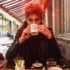 a man sitting at a table drinking from a cup