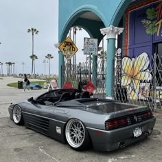 a gray sports car parked in front of a building with graffiti on the walls and palm trees