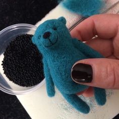 a hand holding a small blue teddy bear in front of a black and white object