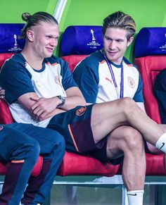 two men sitting on a bench with their legs crossed and one man wearing white socks