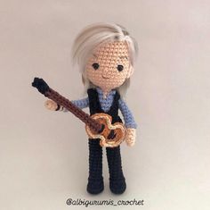 a crocheted doll holding a guitar in it's right hand and wearing a blue shirt