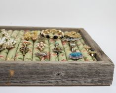 a wooden box filled with lots of different types of rings and brooches on display