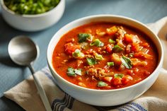 a white bowl filled with soup next to a spoon and some green beans on a blue table cloth