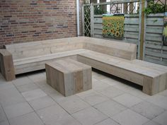 a wooden bench sitting on top of a tiled floor next to a brick wall and fence