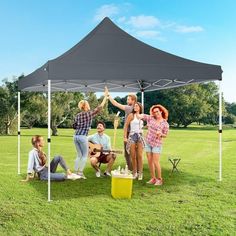 a group of people standing under a tent on top of a grass covered field next to a yellow trash can