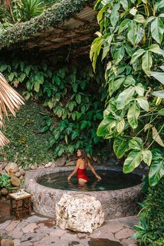 a woman in a red swimsuit is sitting in a hot tub surrounded by greenery