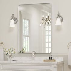 a white bathroom with a large mirror above the sink and chandelier on the wall