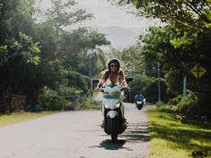 a woman riding on the back of a scooter down a road next to trees