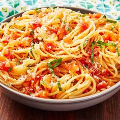 a bowl full of pasta with tomatoes and parmesan cheese on the top, sitting on a wooden table