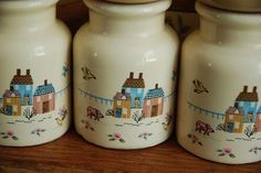 three white jars with houses painted on them sitting on a wooden table next to each other