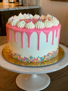 a white cake with pink icing and sprinkles on a gold plate