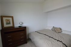 a bed sitting next to a wooden dresser in a white room with tile flooring