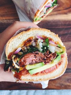 a person holding a sandwich with meat and vegetables