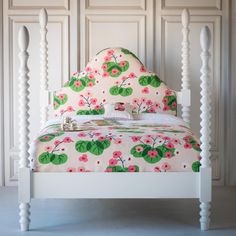 a white bed with pink flowers and green leaves on the headboard is in front of a paneled wall