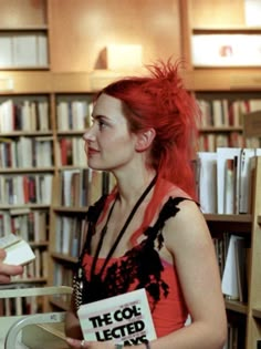 a woman with red hair standing in front of a bookshelf holding a book