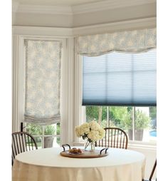 a dining room table with chairs and a tray on it in front of two windows