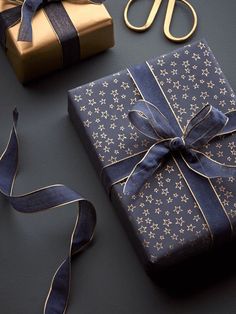 two wrapped presents sitting on top of a table next to scissors and ribbon tied around them