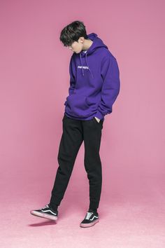 a young man wearing a purple hoodie and black sweatpants standing against a pink background