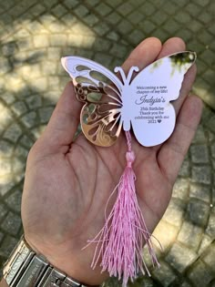 a person holding a butterfly shaped keychain with pink tassels on it