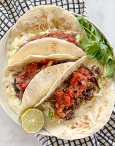 two tacos with meat, lettuce and sauce on a plate next to a lime wedge