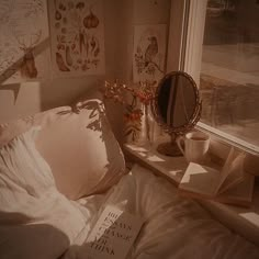 a bed sitting next to a window covered in white sheets and pillow cases with books on top of them