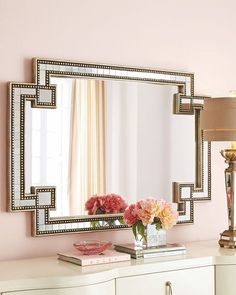 a white dresser topped with a mirror next to a lamp and vase filled with flowers