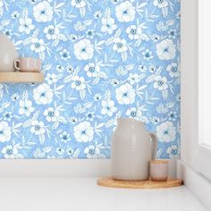 a blue flowered wallpaper with white vases and cups on a shelf in front of it