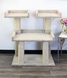 two cat furniture stands in front of a wall with flowers on the floor and a table next to it