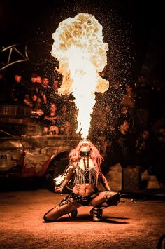 a woman sitting on the ground in front of a large object with flames coming out of it