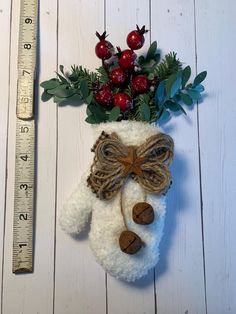 a white stuffed animal with holly and berries on it's head next to a ruler