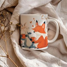 a coffee mug with foxes on it sitting on a bed next to dried flowers and white sheets