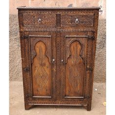 an old wooden cabinet with intricate carvings on the doors and drawers is shown in front of a stucco wall