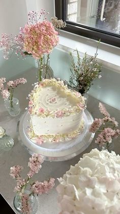 there is a white cake with pink flowers on the table next to other cakes and vases