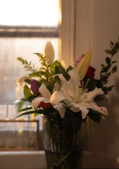 a vase filled with white and red flowers on top of a table next to a window