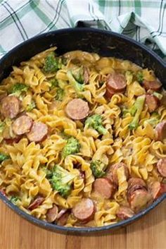 a skillet filled with pasta, sausage and broccoli on top of a wooden table