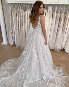 a woman standing in front of wedding gowns and looking at the back of her dress