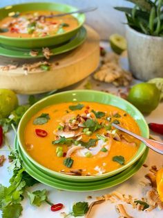 two green bowls filled with soup and garnished with cilantro, limes, red pepper, and peanuts