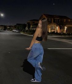 a woman standing in the middle of an empty street at night with her hand on her hip