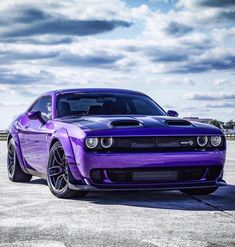 a purple car is parked in an empty lot with cloudy skies behind it and clouds overhead