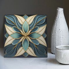 a white vase sitting next to a decorative tile