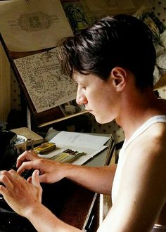 a young man is typing on an old typewriter in his home office with papers scattered about him