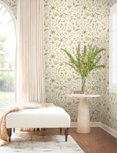 a white bench sitting in front of a window next to a vase filled with flowers