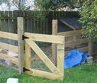 a wooden fence with a blue tarp on the grass in front of it and an animal pen behind it