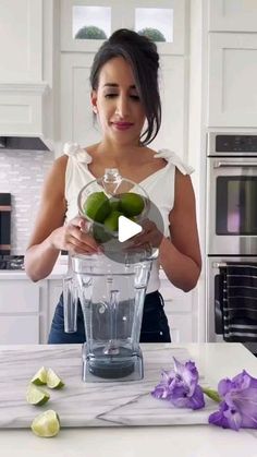 a woman standing in front of a blender filled with limes and cucumbers