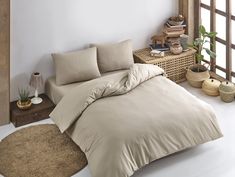 a bed with beige sheets and pillows next to a wooden shelf filled with potted plants