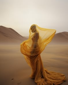 a woman in an orange dress standing on sand dunes with her veil blowing in the wind