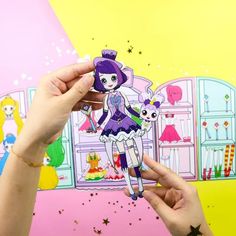 a person holding up a paper doll in front of a wall with dolls on it