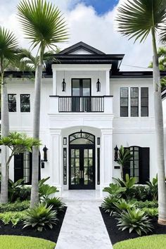 a large white house with black shutters and palm trees in front of the door